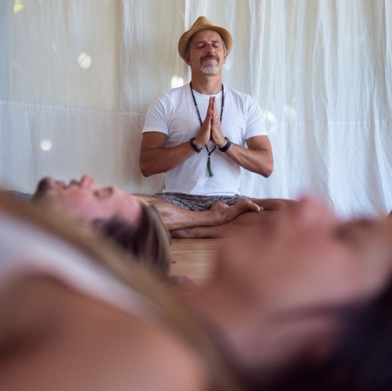 Participants lie on te floor during a Breathwork Session, Facilitator sits crosslegged on the Backgorun