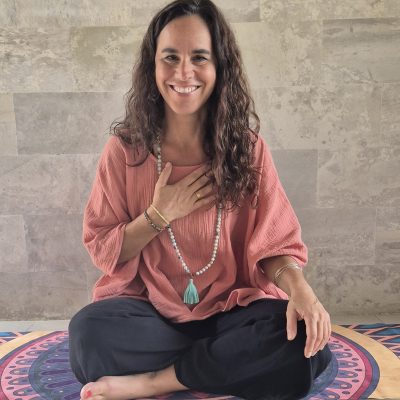 Julia sitzt im Schneidersitz und lächelt zum Camera mit einer Hand am Herzen